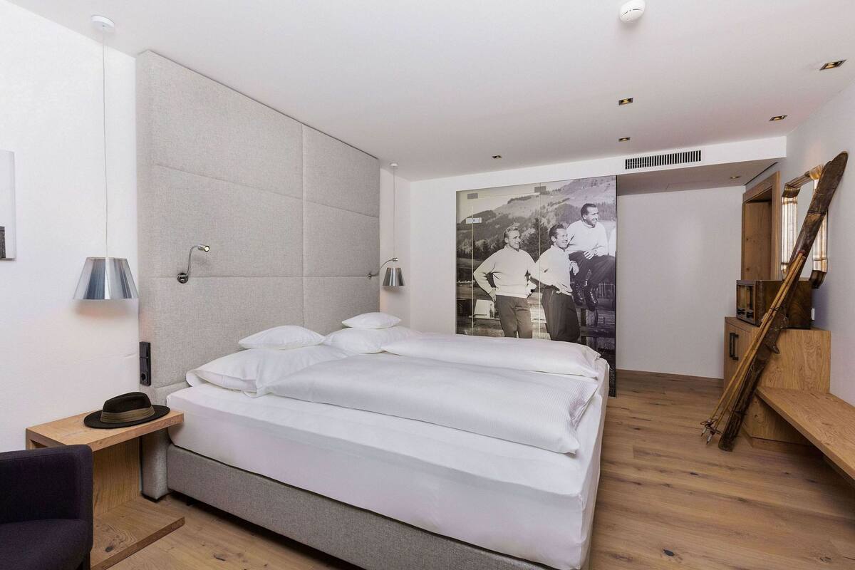 A modern bedroom with a large bed, a wooden nightstand, a desk, and a mirror.