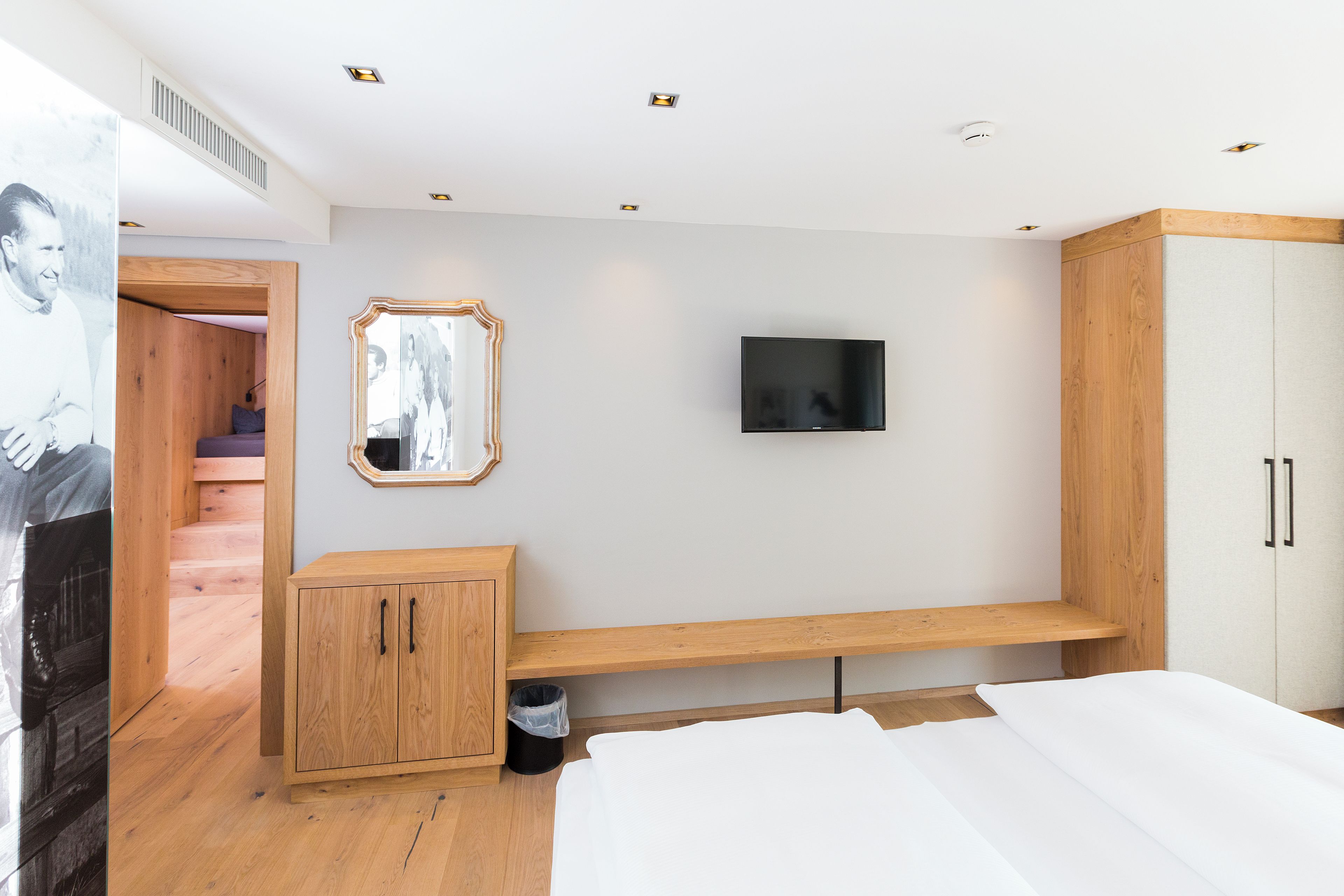 A bedroom with a bed, a TV mounted on the wall, a wooden cabinet, and a mirror.