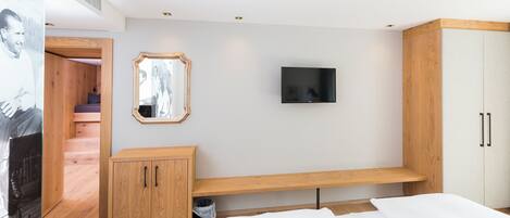 A bedroom with a bed, a TV mounted on the wall, a wooden cabinet, and a mirror.