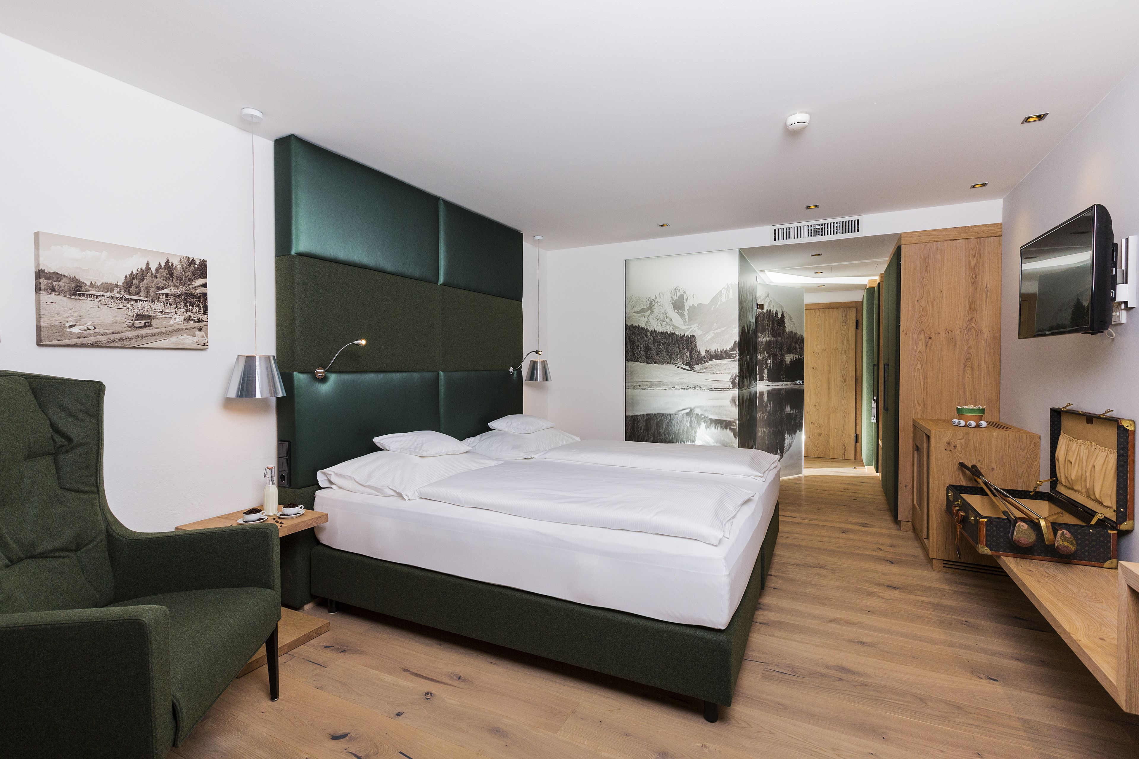 Une chambre d’hôtel moderne avec un grand lit, un fauteuil vert, un bureau en bois et un téléviseur.