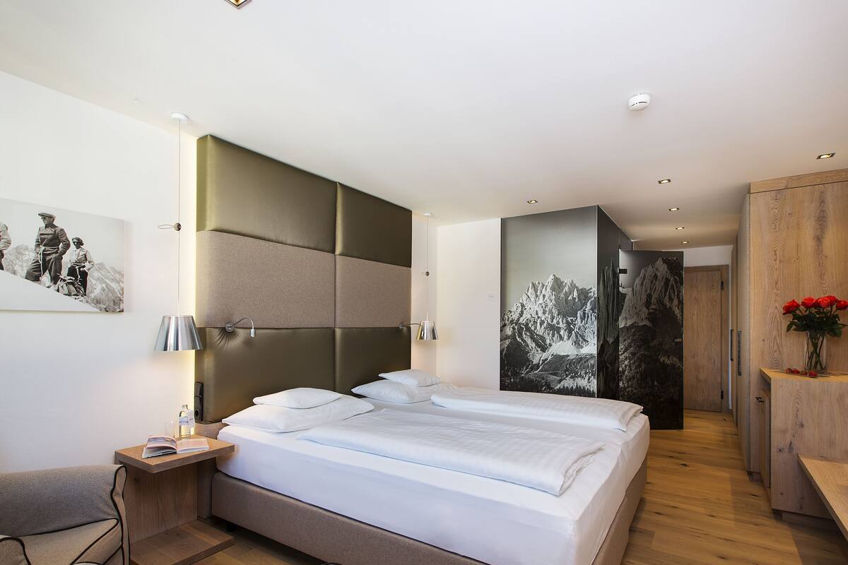 A modern bedroom with a large bed, bedside tables, a wooden wardrobe, and a wall-mounted lamp.