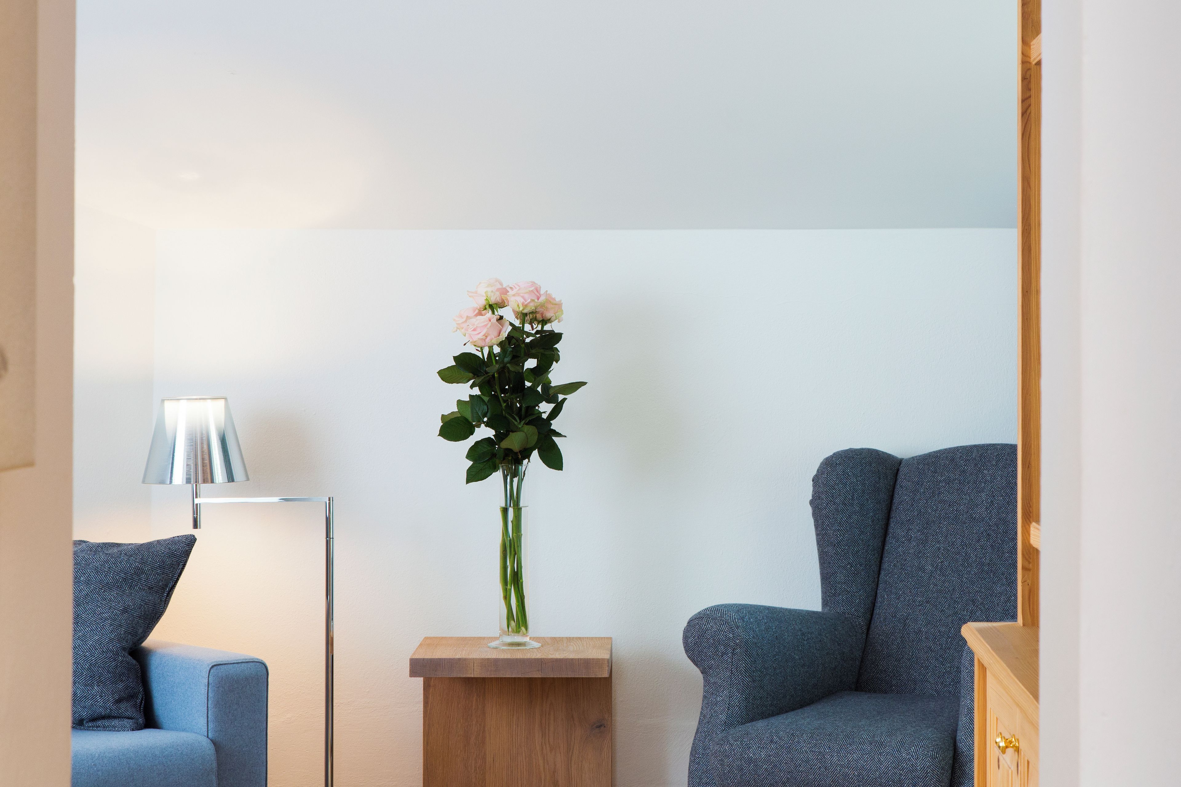 Un salón moderno con un sofá azul, una mesita de madera y un jarrón alto con flores.