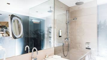 A modern bathroom with a large mirror, a sink, a shower with a handheld showerhead, and a glass-enclosed shower area.