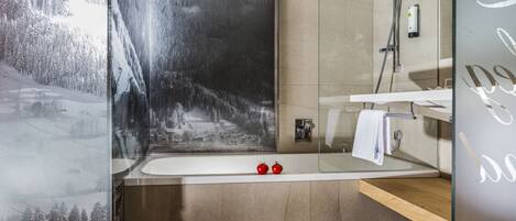 A modern bathroom with a large mirror, a bathtub, and a shower. There is a framed picture of a snowy landscape on the wall.