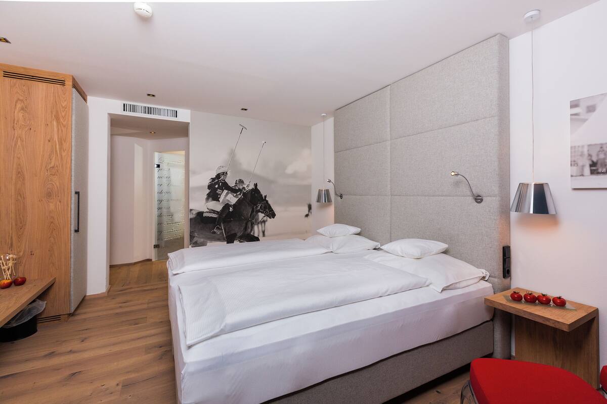 A modern hotel room with a large bed, a wooden wardrobe, and a small table with apples.