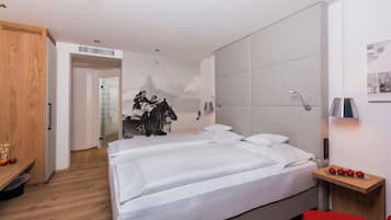 A modern hotel room with a large bed, a wooden wardrobe, and a small table with apples.