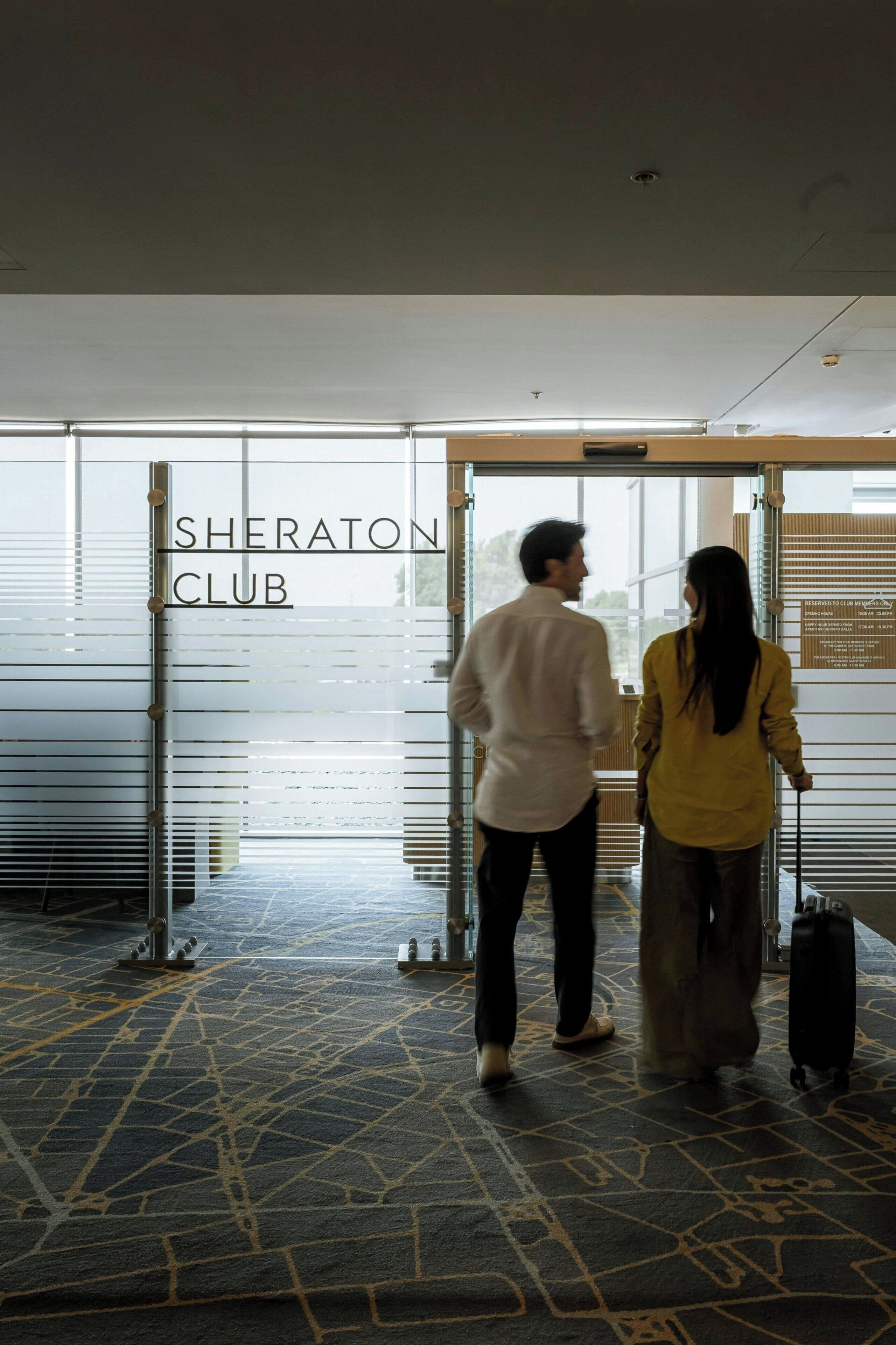 A hotel entrance with a sign reading 'Sheraton Club,' a glass door, and a patterned carpet.