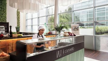 Un interior de restaurante moderno con un chef preparando comida en una barra, ventanas amplias y una pared verde.