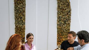 A group of people dining at a table with a white wall and hanging plants in the background.