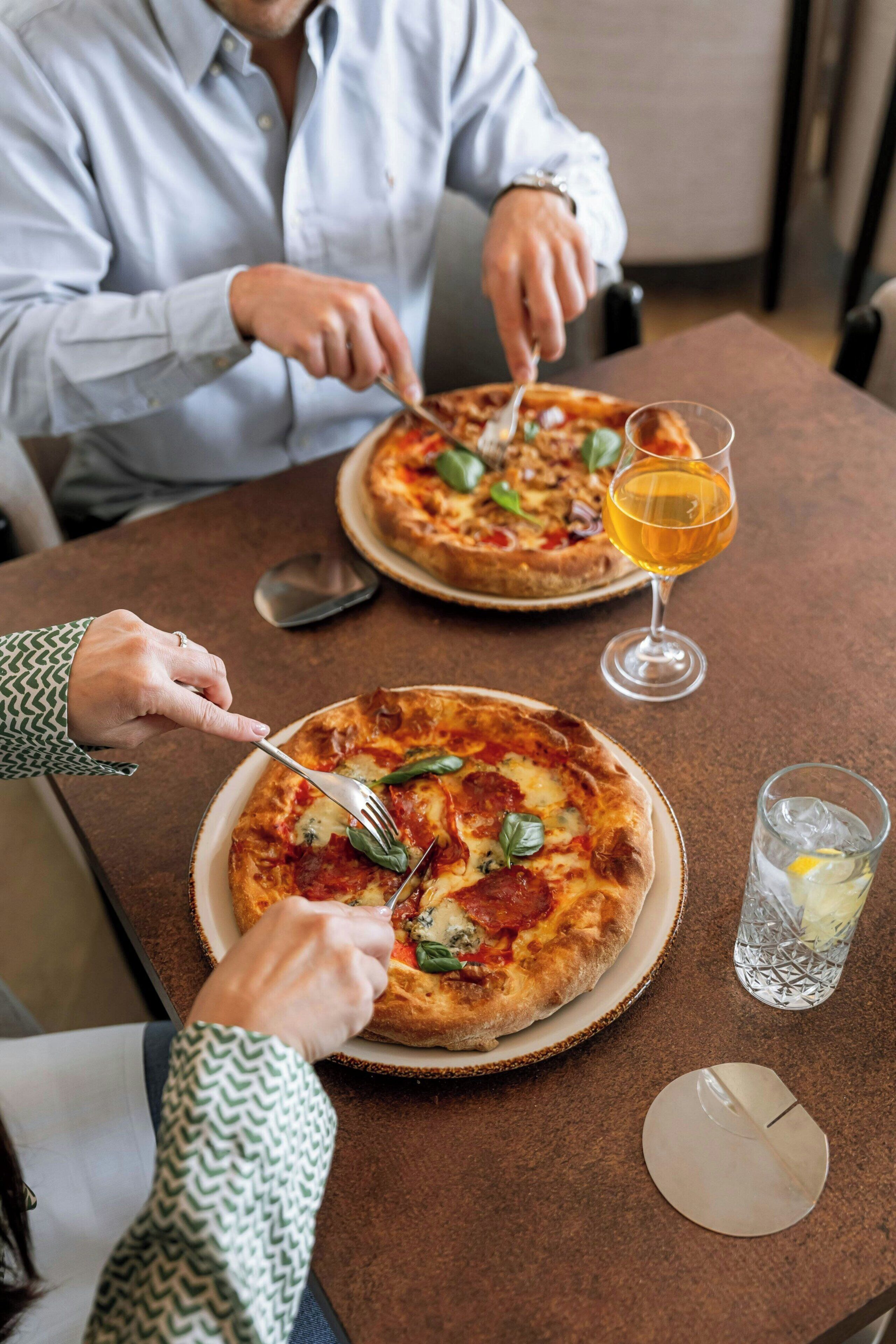 Una mesa de comedor con dos pizzas, una cerveza y un vaso de agua.