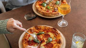 Uma mesa de jantar com duas pizzas, um copo de cerveja e um copo de água.