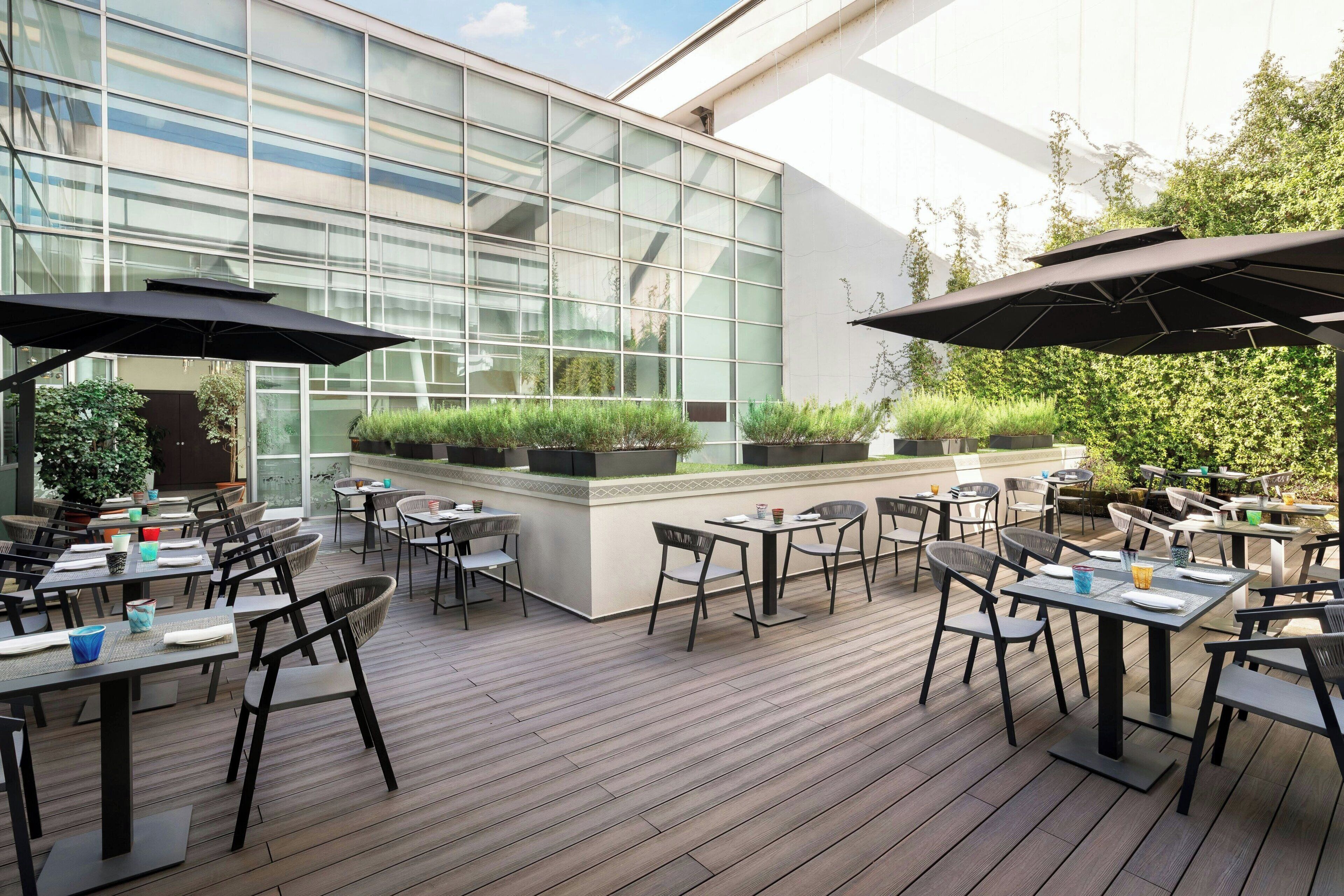 Un patio al aire libre con mesas, sillas, plantas en macetas y sombrillas.