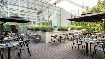 Un patio al aire libre con mesas, sillas, plantas en macetas y sombrillas.