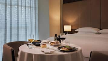 Habitación de hotel con una mesa de comedor lista para una comida, una cama con almohadas y una mesita de noche con lámpara.