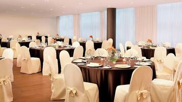 Un salón de banquetes con mesas redondas, sillas blancas adornadas con lazos y centros de mesa florales.