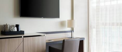 Una habitación de hotel con cama, escritorio, silla, televisión y lámpara.