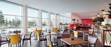 A spacious restaurant with large windows, modern furniture, and a red accent wall.