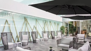 Een modern buitenverblijf met rieten meubilair, glazen wanden en een grote parasol.