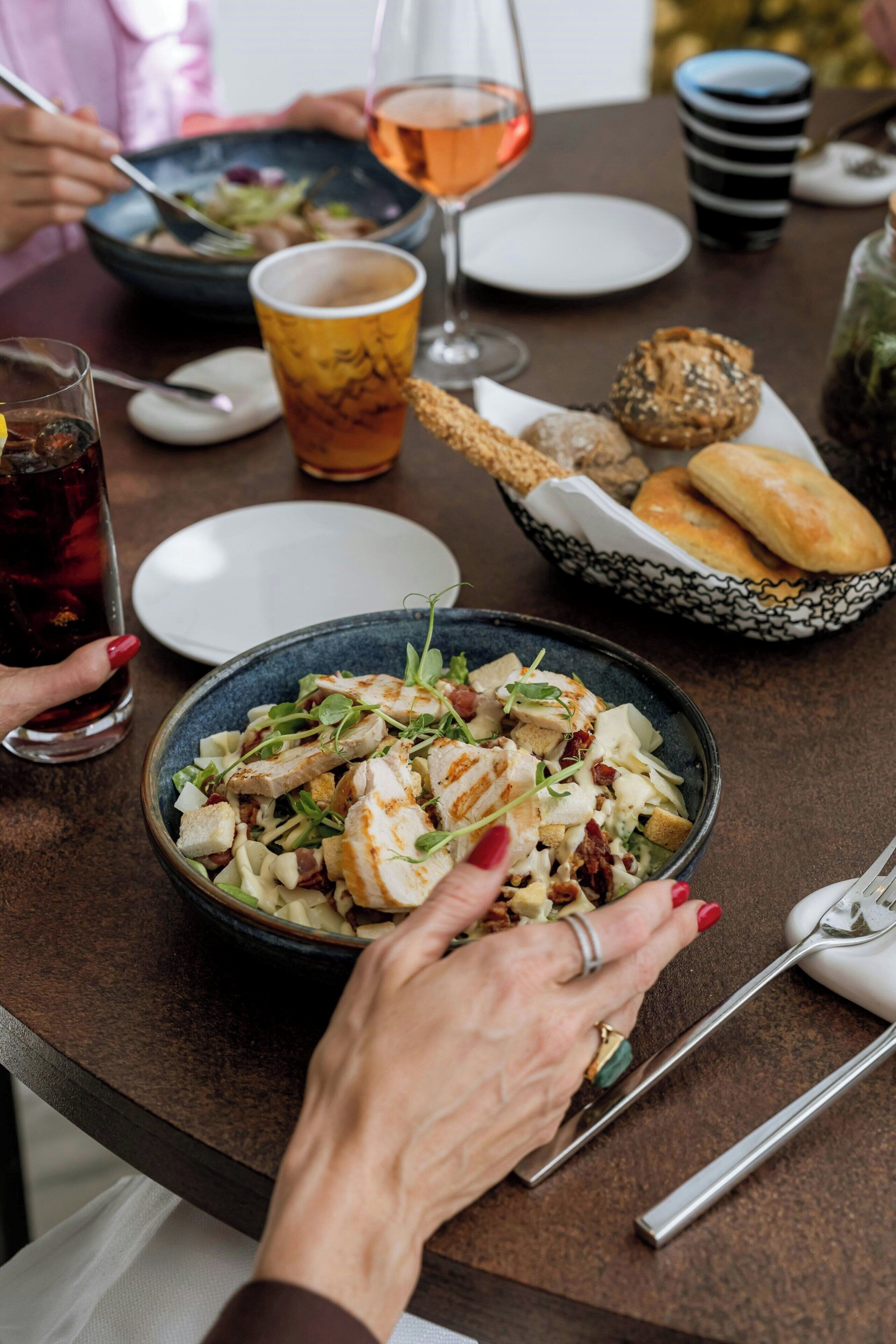 A dining table with a plate of food, a glass of drink, and a basket of bread.