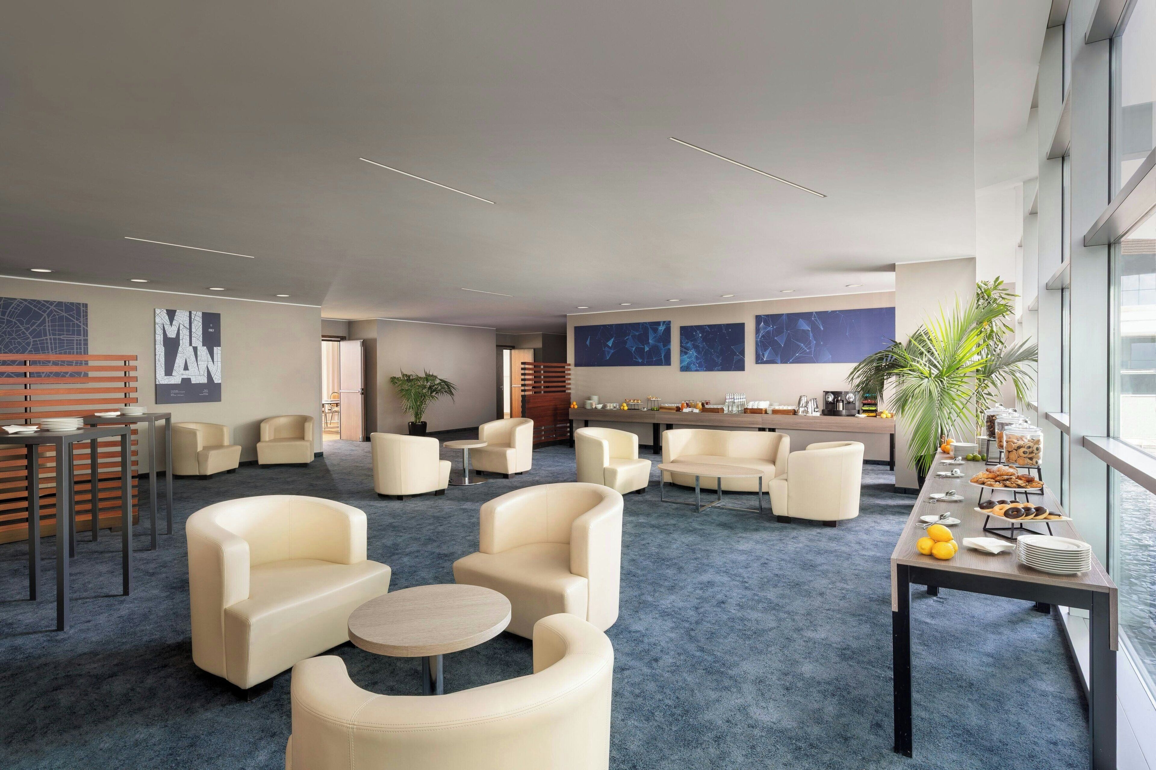 A modern lounge area with sofas, a coffee table, and a buffet table with food and drinks.