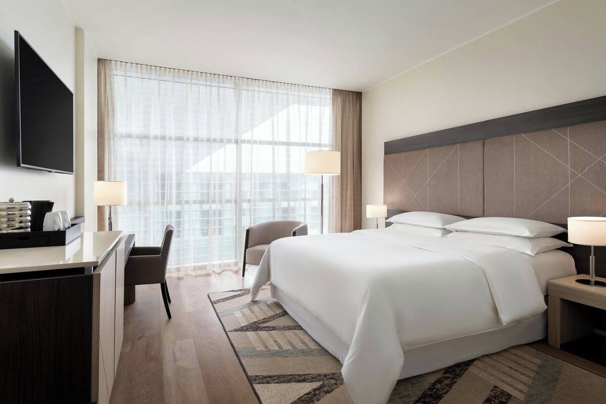 Ein Hotelzimmer mit einem großen Bett, einem Schreibtisch, einem Sessel und einem Fernseher.