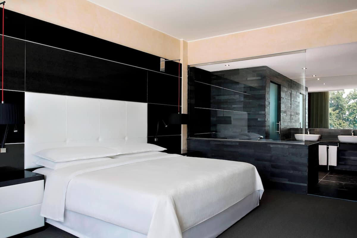 Ein modernes Schlafzimmer mit einem großen Bett, einem Nachttisch, einem Spiegel und einem Badezimmer mit einer Duschkabine aus Glas.