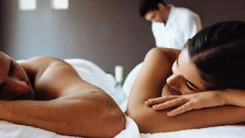 A couple lying in bed with a man in the background.
