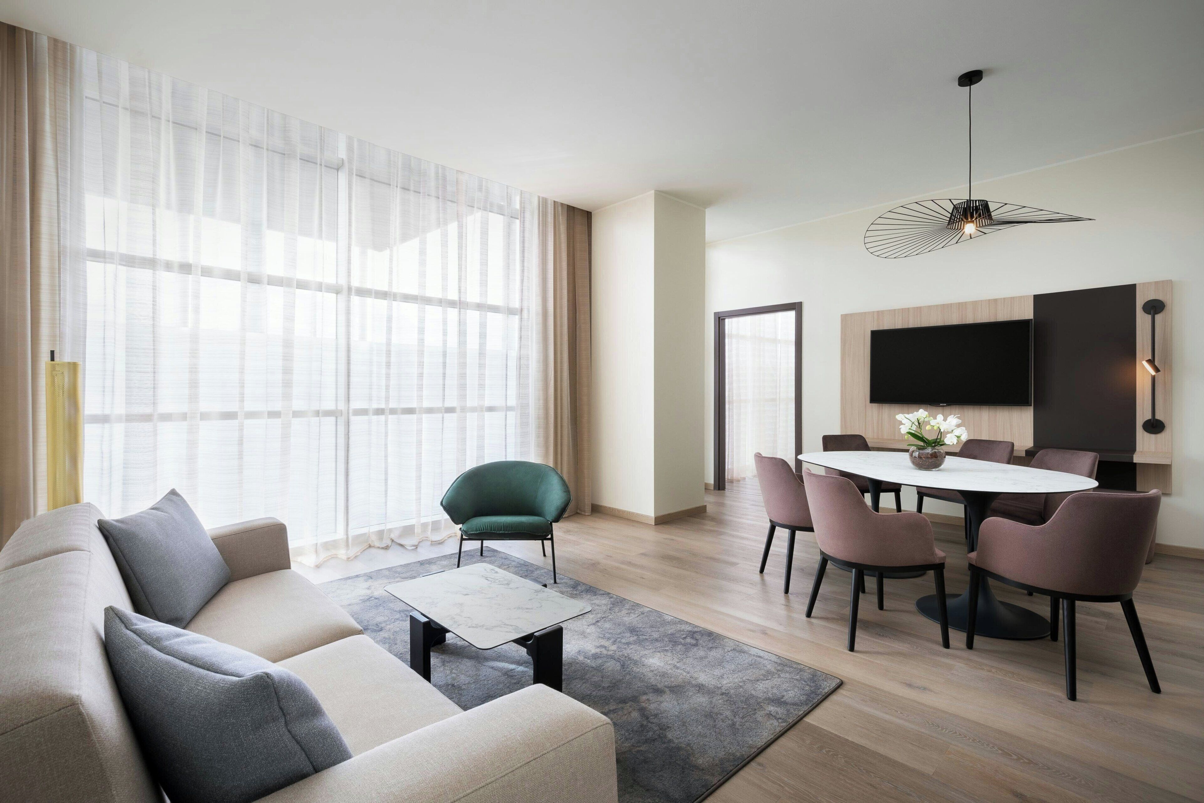 A modern living room with a sofa, coffee table, and dining area with chairs and a TV.