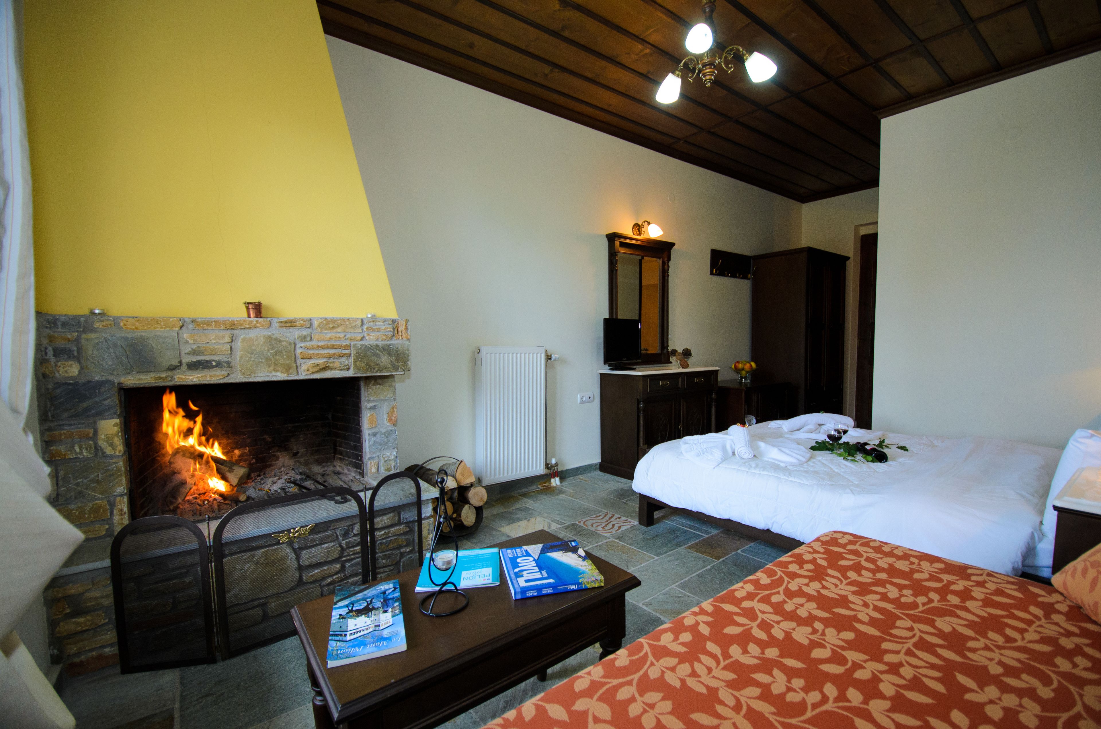 Een kamer met een stenen openhaard, een bed met wit beddengoed, een houten tafel met boeken en een spiegel boven het dressoir.