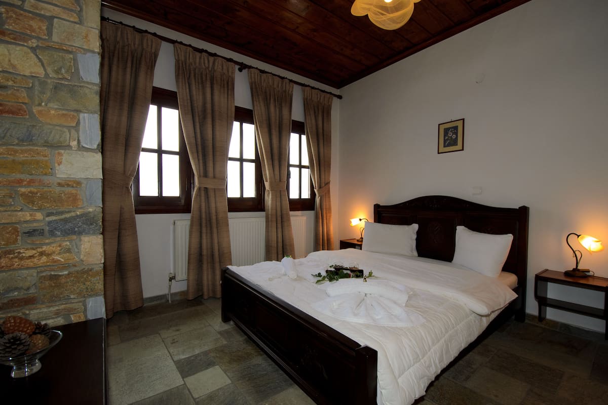 A neatly made bed in a room with stone walls, a wooden ceiling, and two bedside lamps.