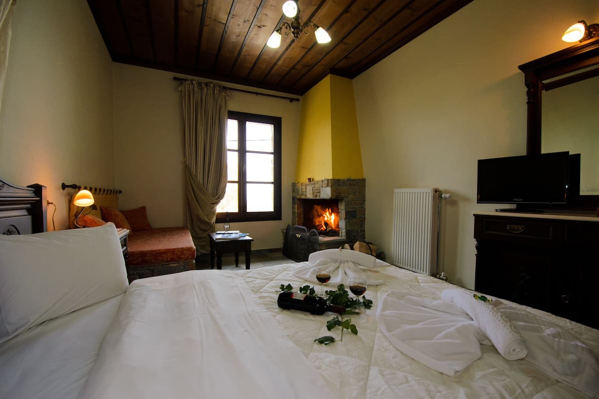 A hotel room with a bed, a fireplace, a television, and a window with curtains.