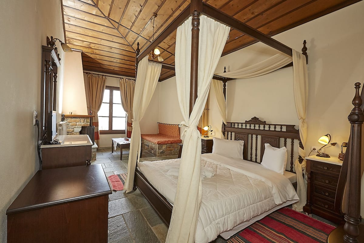 A four-poster bed with a canopy, a wooden dresser, a mirror, and a stone fireplace.