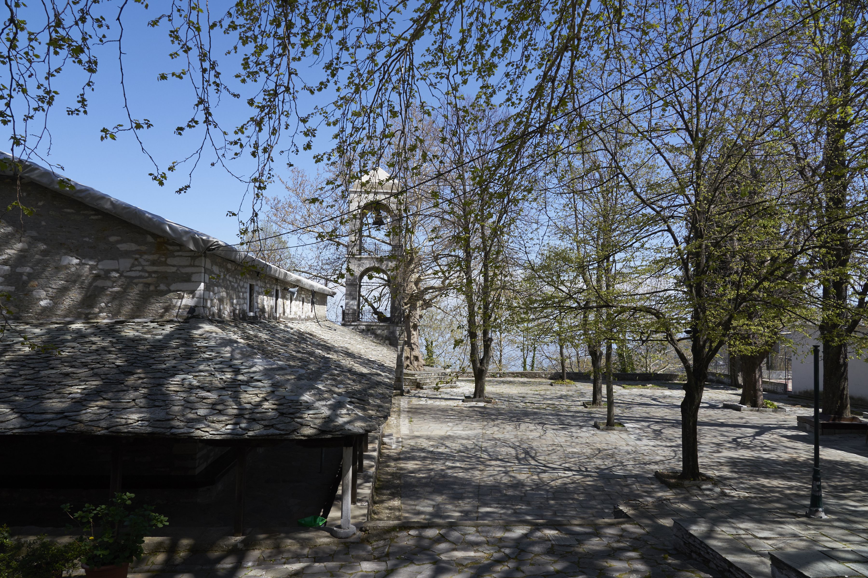 A courtyard with stone buildings, a bell tower, and trees.