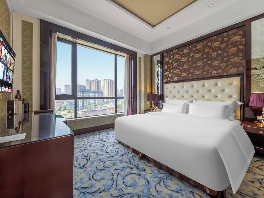Quarto de hotel com uma cama grande, uma escrivaninha e vista para a cidade.