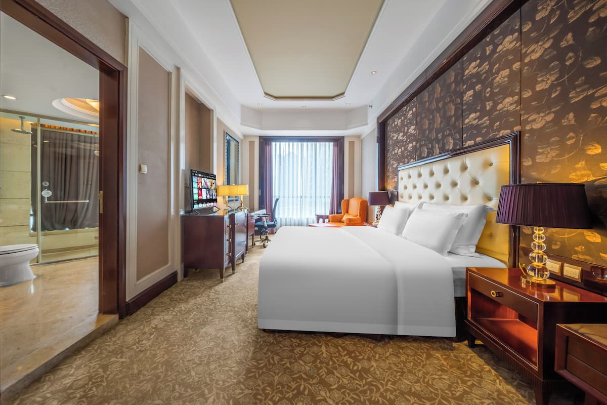 Hotelkamer met een groot bed, een bureau, een stoel, een televisie en een badkamer die door een geopende deur zichtbaar is.