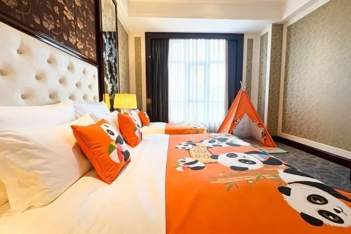 Een hotelkamer met een groot bed, een hoofdbord, een raam met gordijnen, een nachtkastje met een lamp en een decoratief kussen.
