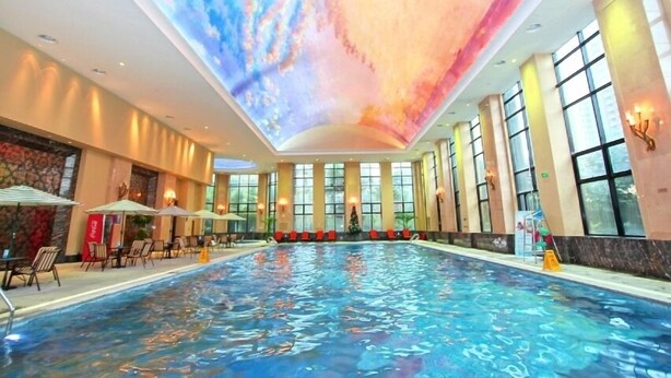 A large indoor swimming pool with a ceiling projection, large windows, and seating areas with umbrellas. - Wyndham Grand Plaza Royale Palace Chengdu (Chengdu)
