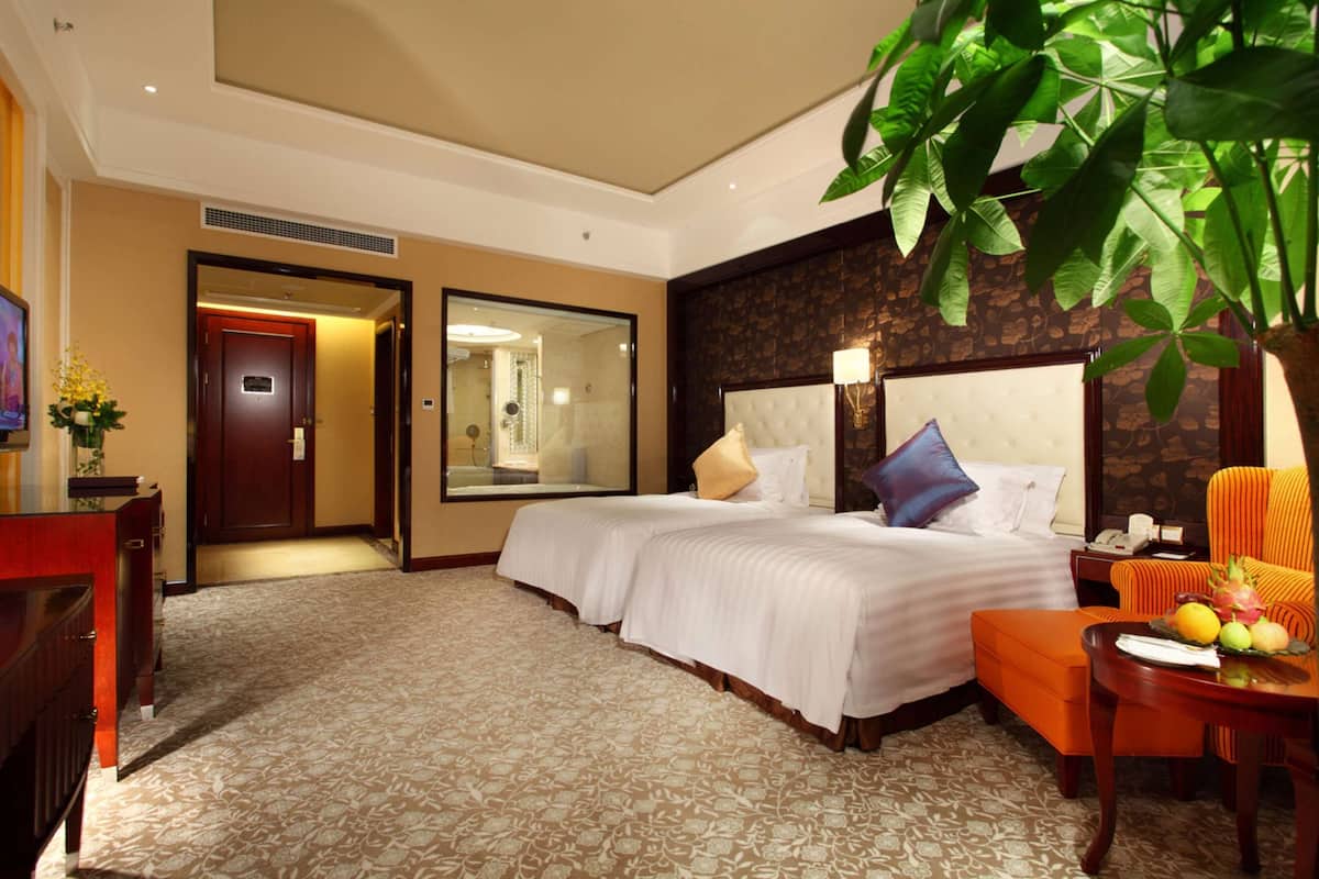 Hotelkamer met een groot bed, een zithoek met een fauteuil, een tafeltje met fruit en een grote plant.