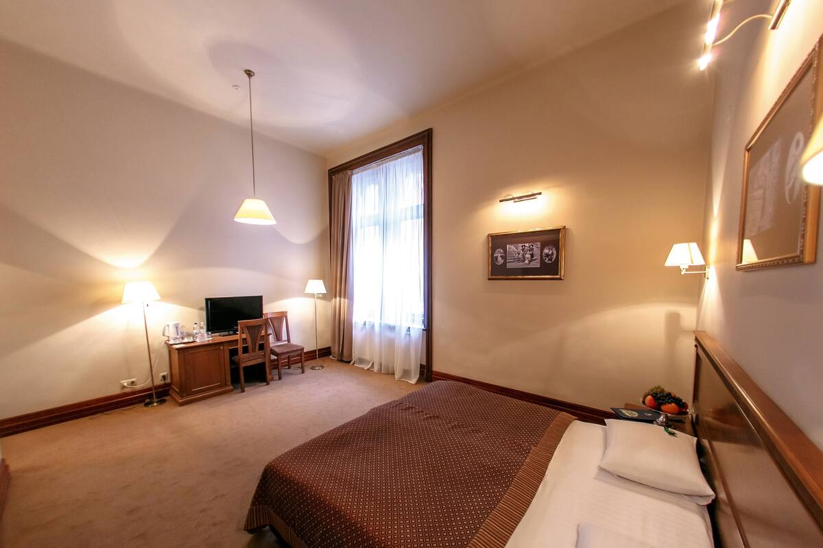 Una habitación de hotel con cama, escritorio con silla, televisor y ventana con cortinas.