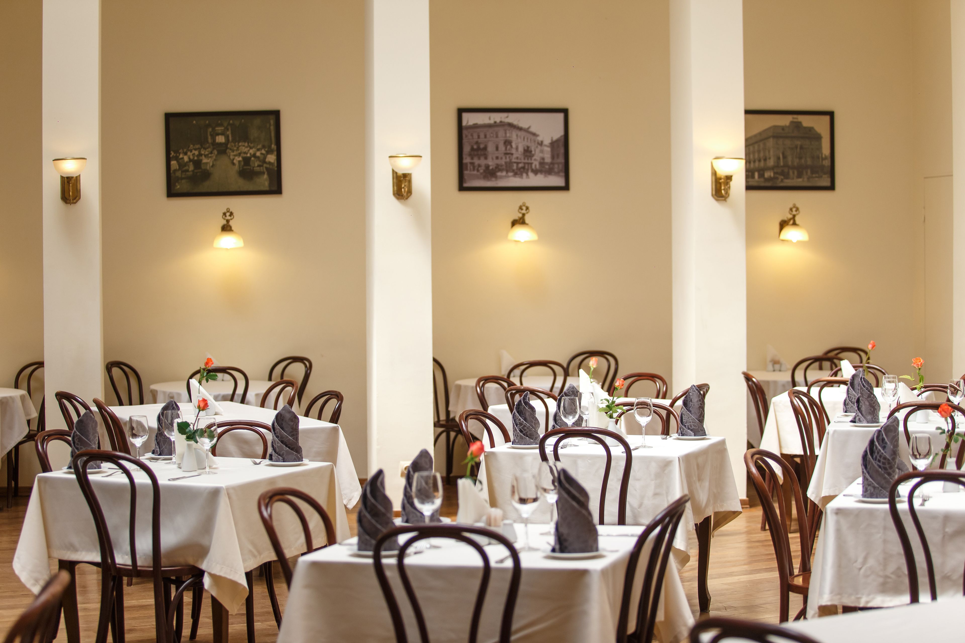A dining area with tables set for service, framed pictures on the walls, and wall-mounted lighting.