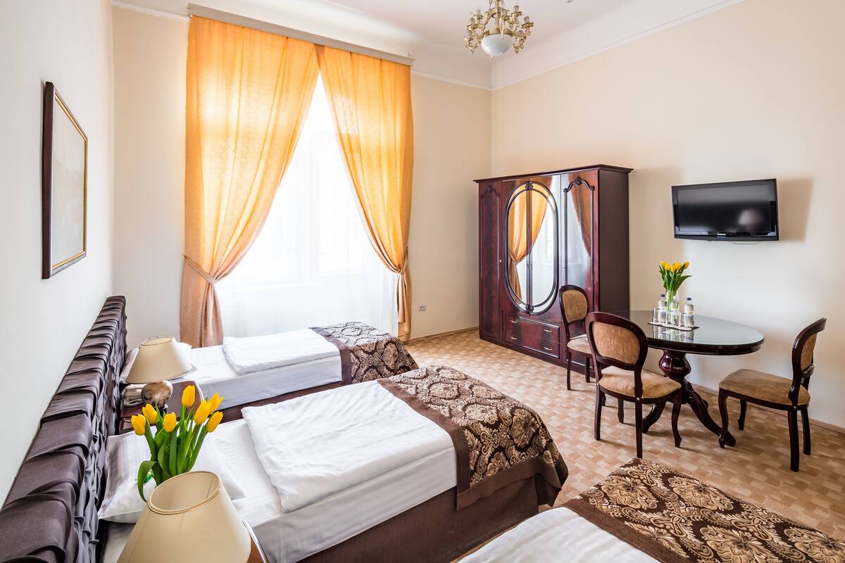Habitación de hotel con dos camas, un sofá, una mesa de comedor con sillas, un televisor y un armario.