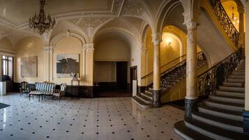 A grand lobby with a tiled floor, a staircase with ornate railings, and a chandelier.