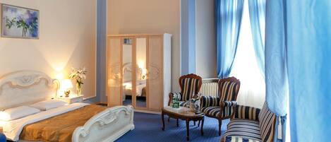 Habitación de hotel con cama, una silla, una mesa y un ventanal con cortinas.