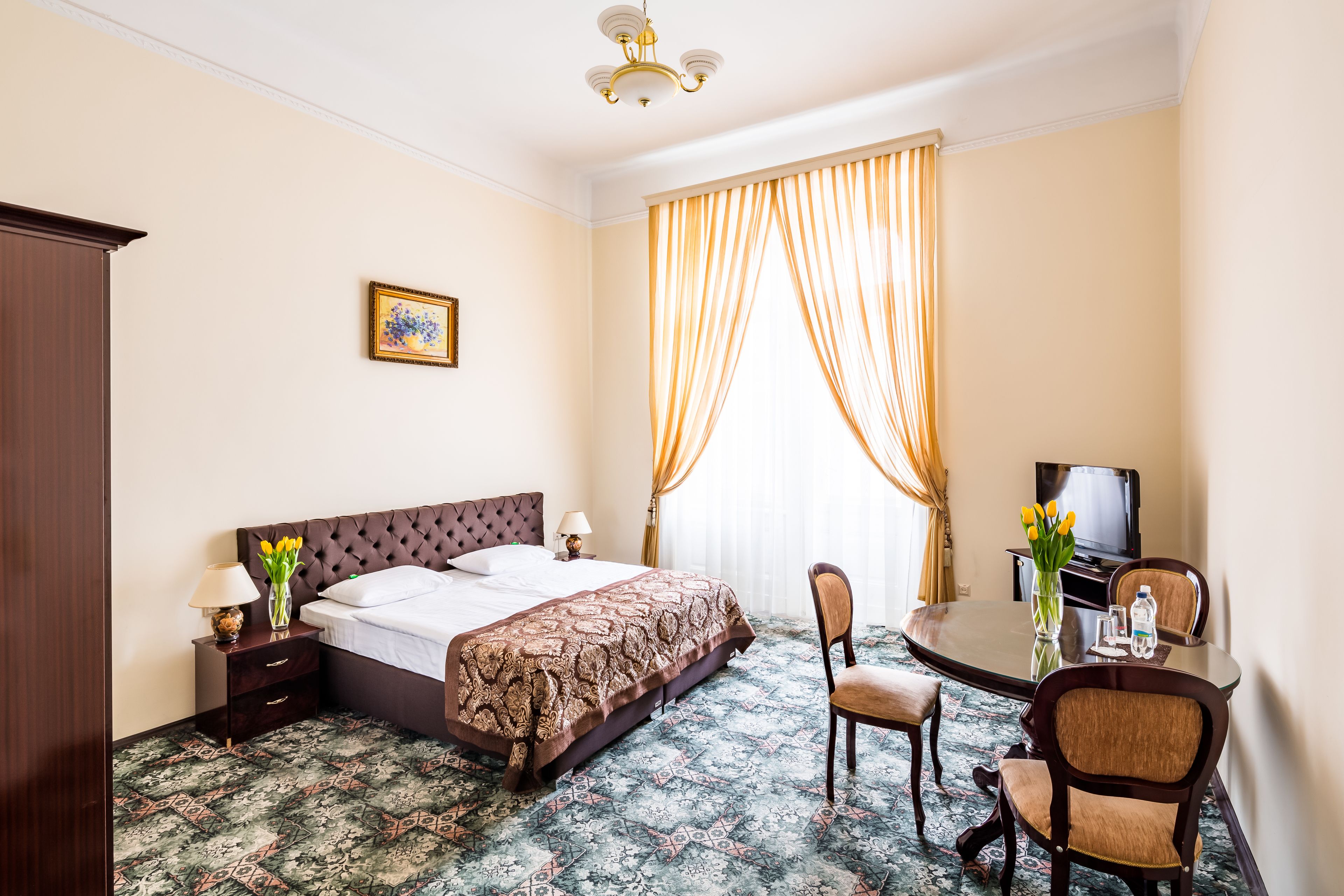 A hotel room with a bed, a desk with a chair, a television, and a window with curtains.