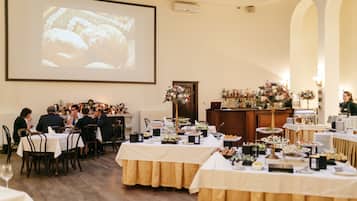 A banquet hall with tables set for a meal, a projection screen, and a bar area with bottles.