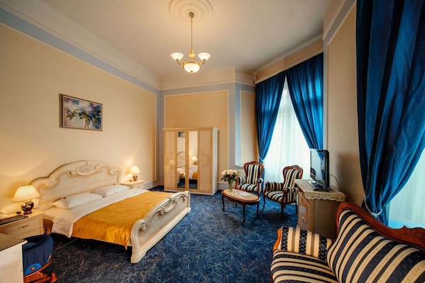 A hotel room with a large bed, a sofa, a desk with a computer, and a chandelier. - George Hotel (Lviv)