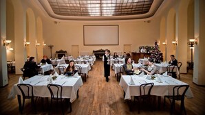A formal dining room with tables set for a meal, a waiter attending to guests, and a Christmas tree in the background. - George Hotel (Lviv)