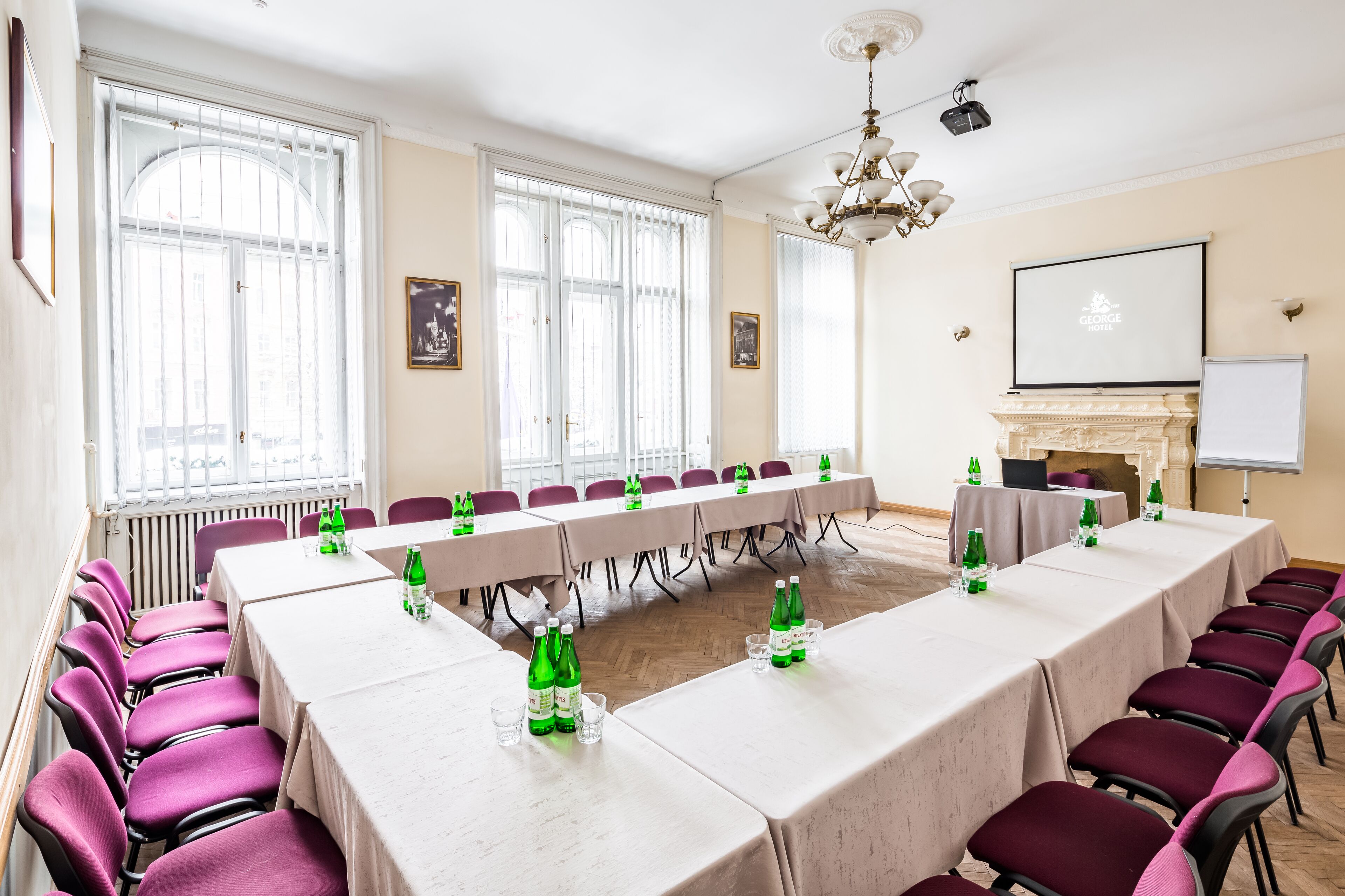 Un salón de conferencias con mesas largas, sillas moradas y botellas de agua verdes.