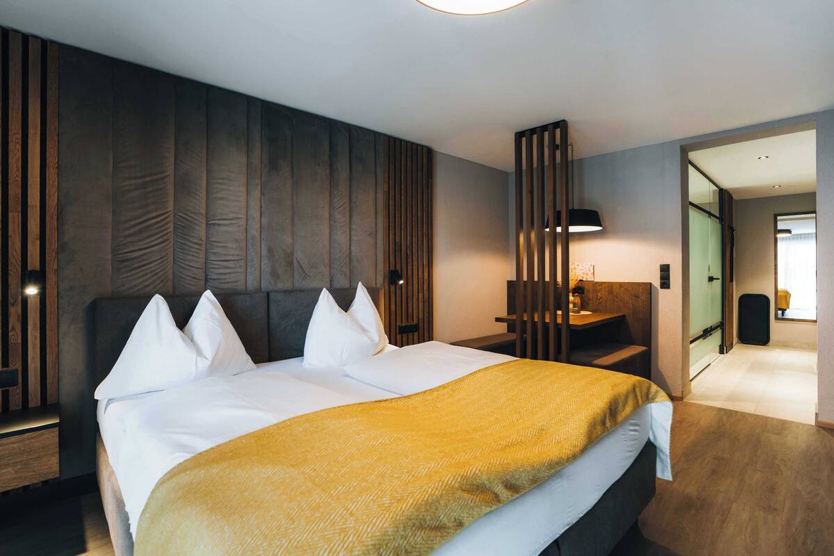 A modern hotel room with a large bed, wooden paneling on the walls, a desk, and a mirror.