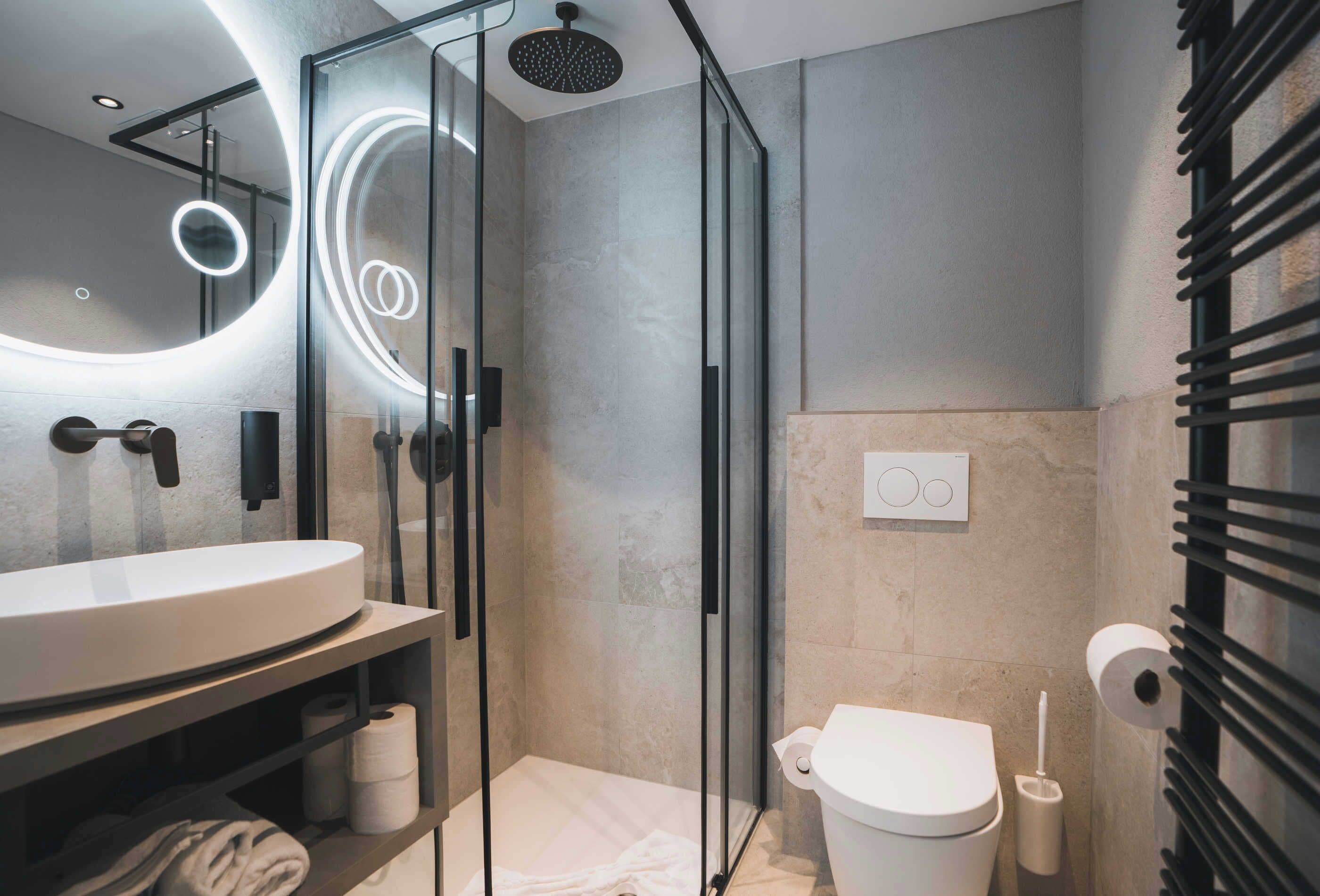 A modern bathroom with a glass-enclosed shower, a white sink, and a toilet.